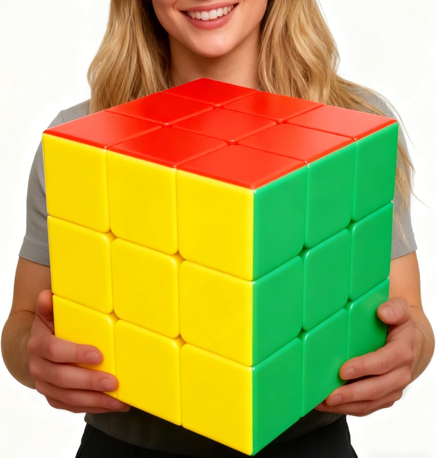 A large oversized Rubik's Cube with bright red, yellow, and green colored squares visible on its three exposed faces, being held by a smiling person wearing a gray shirt.