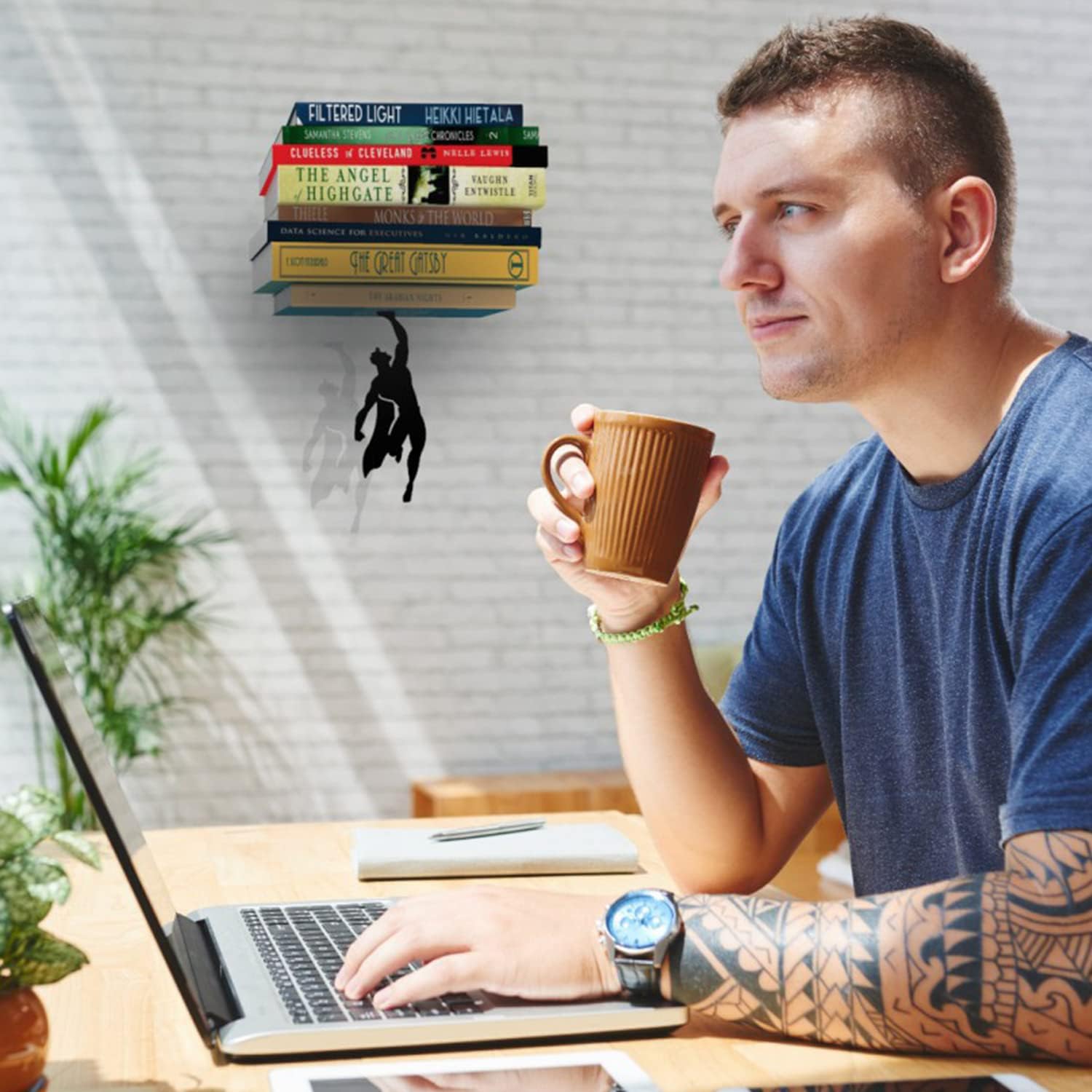A creative wall-mounted bookshelf featuring a silhouette of Superman in a flying pose that suspends a stack of colorful books above, creating the illusion that the superhero figure is holding up the literary collection.