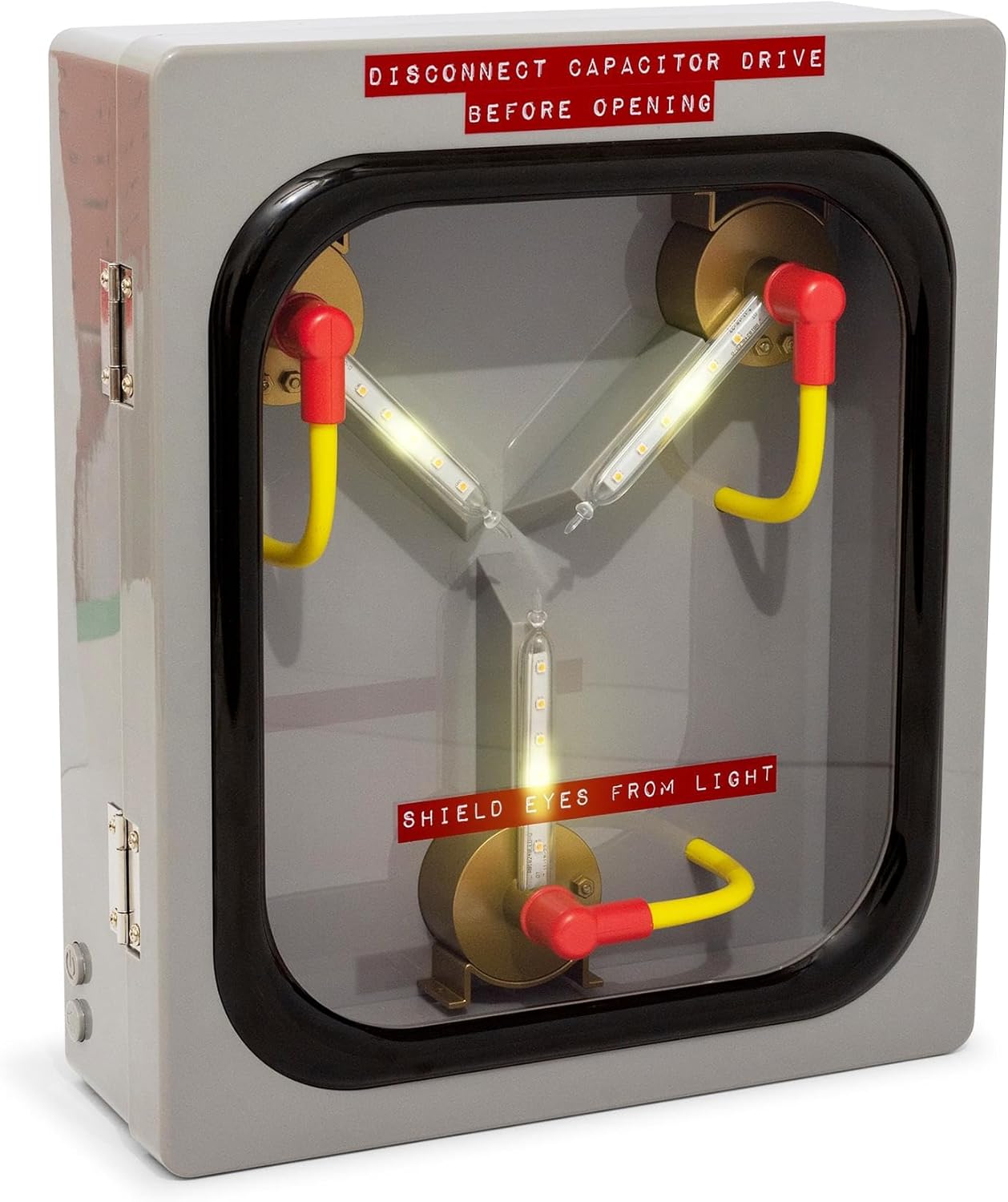 A Flux Capacitor Replica encased in a clear-fronted metal box with warning labels, featuring illuminated tube components and red and yellow handles mounted on brass fixtures.