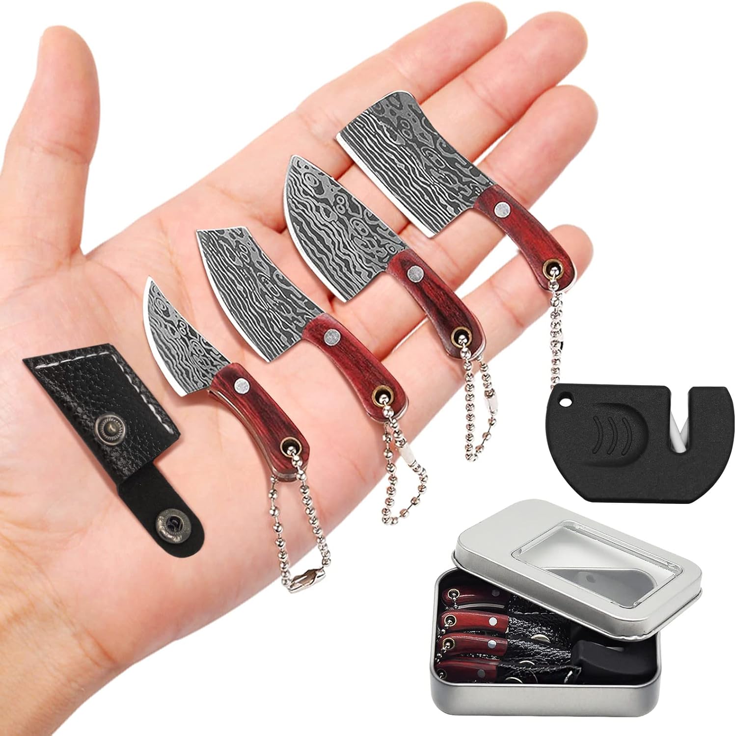 Four miniature Damascus steel keychain knives with dark wood handles and metal chains, displayed in an open palm alongside a black sharpener and silver metal storage tin.